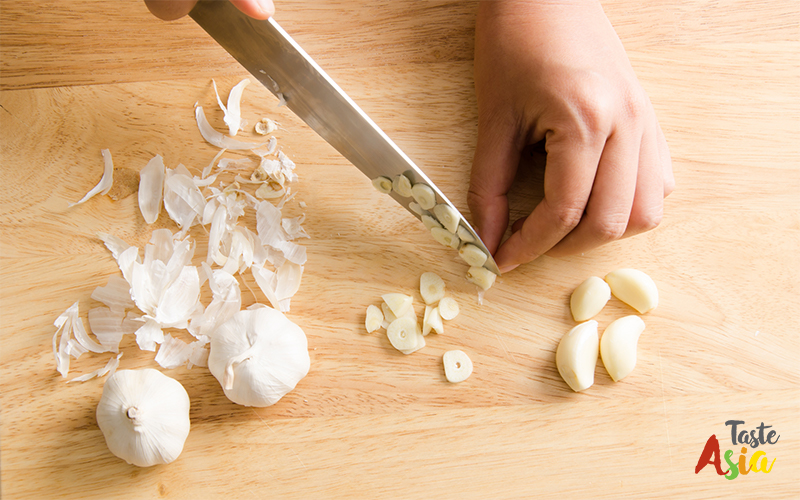 Woman slices garlic on wooden board for cooking