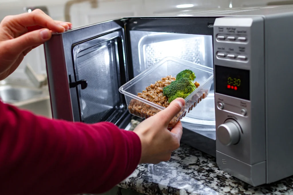 woman hand puts plastic container with brocolli buckwheat microwave